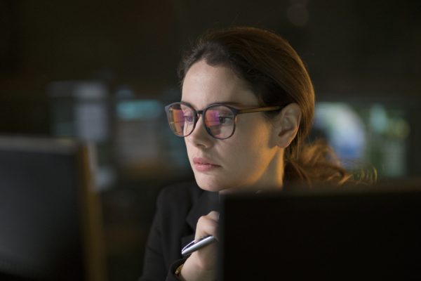 Stock photo of a good looking professional woman contemplating the content of a computer display in a dark office.