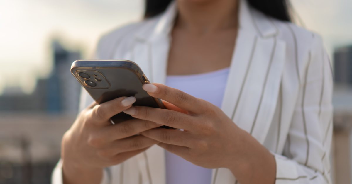 Close-up of a mobile phone in the hands of a woman in a striped jacket and white top on the street, selective focus.