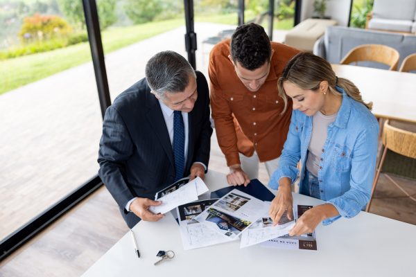 Latin American couple looking at the blueprints of a house and asking questions to the real estate agent
